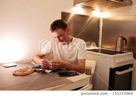 A man sits at the table and carefully prepares a hand rolled cigarette. The concept highlights a quiet personal routine and focused manual work A man sits at the table and carefully prepares a hand rolled cigarette. The concept highlights a quiet personal routine and focused manual work 135253068