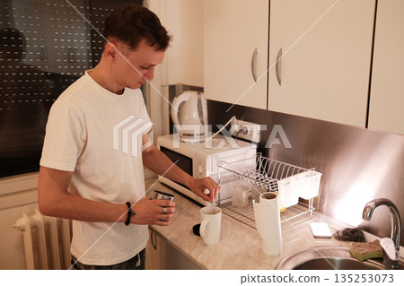 A man stirs coffee in a cup while standing in the kitchen. The scene represents a soothing morning ritual concept A man stirs coffee in a cup while standing in the kitchen. The scene represents a soothing morning ritual concept 135253073