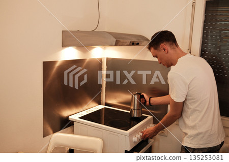 A man places a moka pot on the stove to brew coffee. The scene reflects a warm and comforting morning concept A man places a moka pot on the stove to brew coffee. The scene reflects a warm and comforting morning concept 135253081