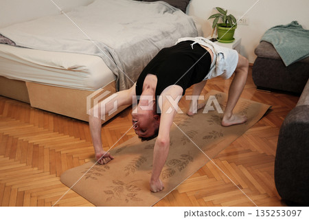 A man performs a bridge pose on a yoga mat at home. The moment expresses active stretching concept A man performs a bridge pose on a yoga mat at home. The moment expresses active stretching concept 135253097