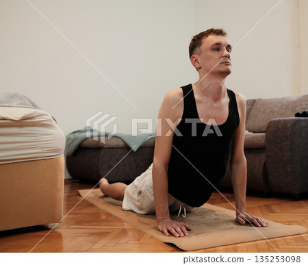 A man performs a cobra yoga pose on a mat in his bedroom. The scene highlights morning stretching concept A man performs a cobra yoga pose on a mat in his bedroom. The scene highlights morning stretching concept 135253098