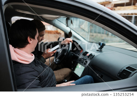 Two men sit inside a car while one checks information on a smartphone. The scene reflects navigation, planning, and road assistance Two men sit inside a car while one checks information on a smartphone. The scene reflects navigation, planning, and road assistance 135253254