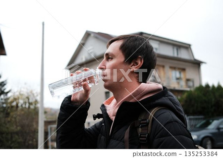 A man drinks water from a bottle during a walk. The moment shows daily routine and urban lifestyle 135253384