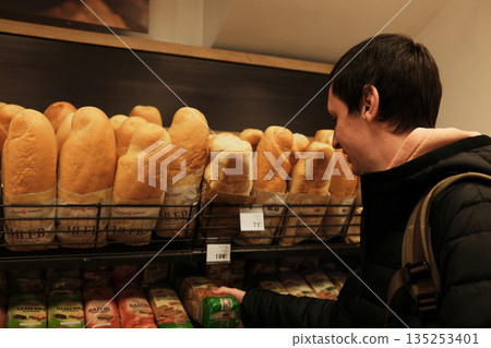A man selects packaged bread in a bakery aisle. The scene shows everyday grocery shopping and routine food decisions A man selects packaged bread in a bakery aisle. The scene shows everyday grocery shopping and routine food decisions 135253401