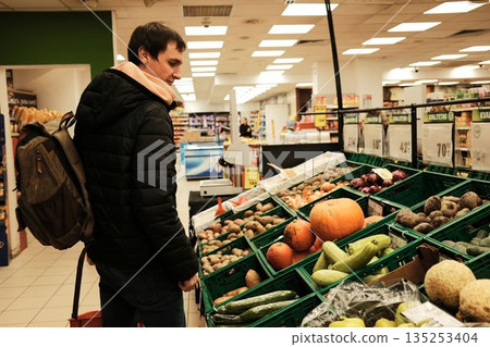 A man stands by a vegetable display in a supermarket. The scene reflects daily shopping and mindful food choices A man stands by a vegetable display in a supermarket. The scene reflects daily shopping and mindful food choices 135253404