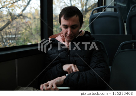 A man sits by the bus window and looks at his watch. The moment reflects routine commuting and the concept of daily scheduling A man sits by the bus window and looks at his watch. The moment reflects routine commuting and the concept of daily scheduling 135253408