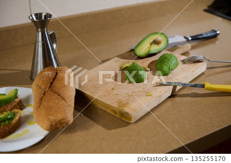 Avocado Prep On Wooden Cutting Board With Bread, Knife And Olive Oil Jug 135255170