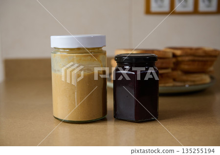 Peanut Butter And Jam Jars On Kitchen Counter With Pancake Stack In Background 135255194