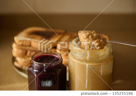 Cozy Breakfast Scene With Toast, Peanut Butter, And Jam In Glass Jars On a Plate 135255198