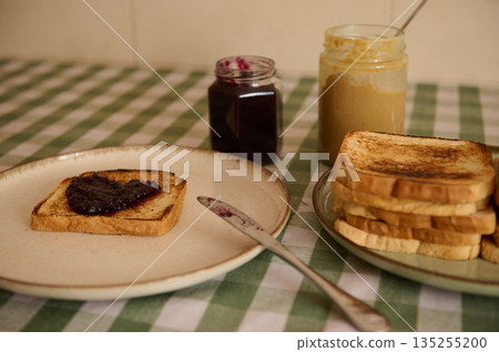 Toast With Jam On Plate, Jars Of Jam And Peanut Butter On Checkered Tablecloth Toast With Jam On Plate, Jars Of Jam And Peanut Butter On Checkered Tablecloth 135255200