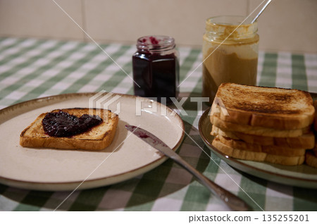 Toast With Jam, Buttered Bread, And Jars On Checkered Tablecloth Breakfast Scene Toast With Jam, Buttered Bread, And Jars On Checkered Tablecloth Breakfast Scene 135255201