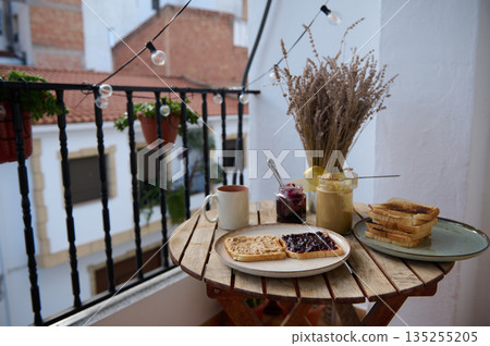 Cozy Balcony Breakfast With Toasts, Jam, And Tea On A Wooden Table With Dried Flowers Cozy Balcony Breakfast With Toasts, Jam, And Tea On A Wooden Table With Dried Flowers 135255205