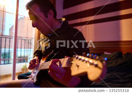 Man Playing Electric Guitar In Cozy Room With Sunset Light On Balcony 135255318