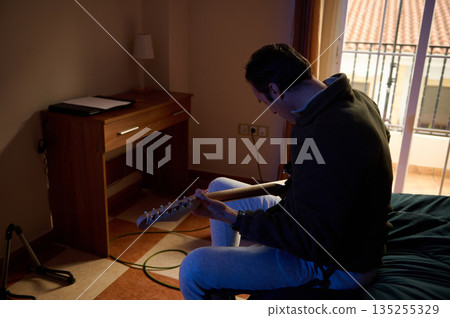Man Playing Electric Guitar In Cozy Hotel Room By Balcony Window 135255329