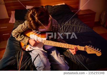 Young Musician Plays Electric Guitar in Cozy Bedroom, Relaxed Home Practice Session Young Musician Plays Electric Guitar in Cozy Bedroom, Relaxed Home Practice Session 135255340