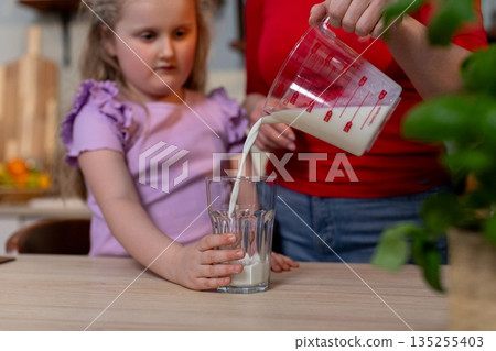 Milk pouring scene, Focus on pouring milk into bottle on countertop with child watching, Detailed view of milk flowing into bottle while child observes in background Milk pouring scene, Focus on pouring milk into bottle on countertop with child watching, Detailed view of milk flowing into bottle while child observes in background 135255403
