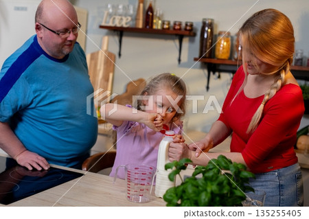 Family cooking together, Parents and child baking happily, Child helps with cooking as parents supervise, Child assisting in kitchen under parental guidance and encouragement 135255405