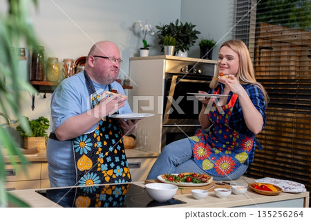 Couple reviews meal expressively, Man and woman sample dish with enthusiasm, Caucasian man and woman passionately taste and review prepared dish in relaxed kitchen setting Couple reviews meal expressively, Man and woman sample dish with enthusiasm, Caucasian man and woman passionately taste and review prepared dish in relaxed kitchen setting 135256264