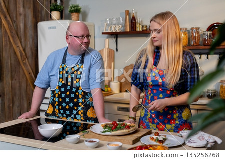 Pair carefully placing dishes and utensils in cozy kitchen environment, Two individuals collaborate to arrange dining items while preparing for pleasant evening together Pair carefully placing dishes and utensils in cozy kitchen environment, Two individuals collaborate to arrange dining items while preparing for pleasant evening together 135256268