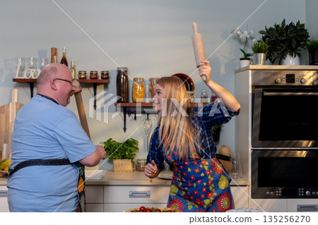 Joyful couple teasing in kitchen, Vibrant scene of lovers teasing amid kitchen utensils, An energetic couple engaging in cheerful mock quarrel using cooking accessories Joyful couple teasing in kitchen, Vibrant scene of lovers teasing amid kitchen utensils, An energetic couple engaging in cheerful mock quarrel using cooking accessories 135256270