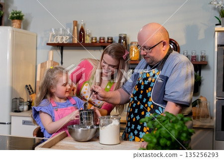 Gentle grandfather instructs young one in mixing ingredients carefully, Experienced grandfather demonstrates how to blend batter while young child observes attentively 135256293