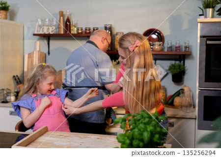 White family playfully baking in kitchen, two girls tugging wooden spoon while grandfather laughs, flour on counter, warm morning light, cozy domestic atmosphere 135256294