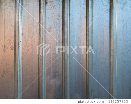 Corrugated metal wall reflecting natural light with weathered surface providing copy space for industrial texture backgrounds 135257823