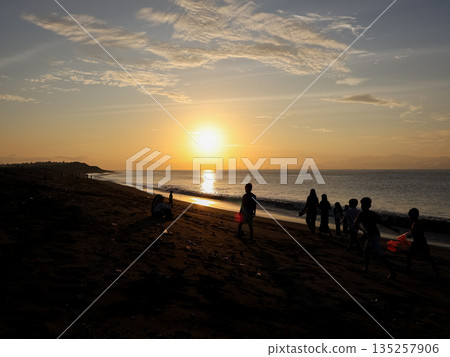 Coastal Sunset with Silhouetted Figures Enjoying Beach Time at Dusk with Natural Light, Creating a Serene and Peaceful Atmosphere for Relaxation and Recreation 135257906