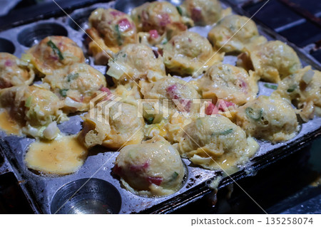 Delicious Takoyaki Cooking in a Pan with Natural Light, Close-Up View of Japanese Octopus Balls Being Prepared for Street Food Vending Delicious Takoyaki Cooking in a Pan with Natural Light, Close-Up View of Japanese Octopus Balls Being Prepared for Street Food Vending 135258074