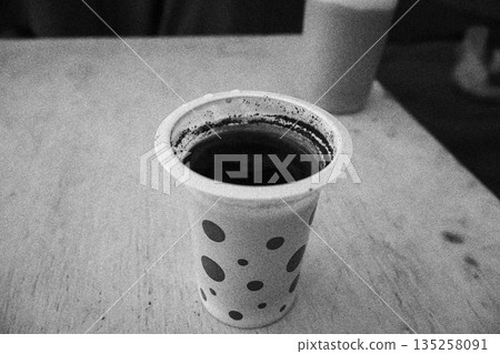 Disposable cup of black coffee sitting on a table with natural light creating authentic mood for simple pleasures and everyday moments 135258091