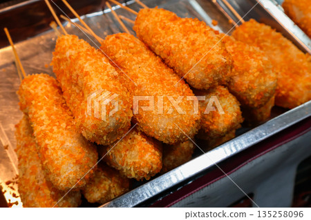 Pile of corn dogs displayed in a tray, coated with crispy orange breading under natural light, perfect for showcasing street food or fair snacks 135258096