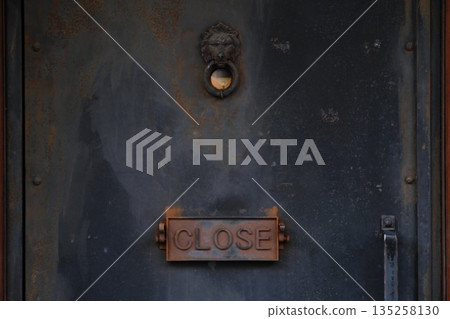 Rusty iron door with a lion door knocker and a CLOSE sign. Antique background material Rusty iron door with a lion door knocker and a CLOSE sign. Antique background material 135258130