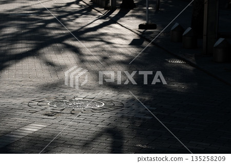 A shadow is cast on a manhole cover on a street corner 135258209