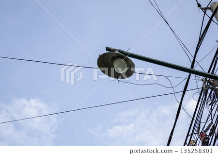 Streetlight against blue sky and tangled wires providing illumination in urban area, natural light with ample copy space for text overlay Streetlight against blue sky and tangled wires providing illumination in urban area, natural light with ample copy space for text overlay 135258301