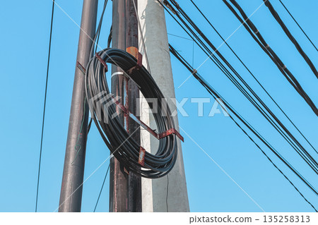 Roll of black cable hanging on utility pole with blue sky background, used for telecommunications infrastructure development Roll of black cable hanging on utility pole with blue sky background, used for telecommunications infrastructure development 135258313