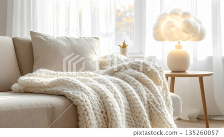 Cozy Minimal Living Room with Knitted Wool Blanket on Sofa, White Window and Sheer Curtains, Decorated with Cloud Lamp Cozy Minimal Living Room with Knitted Wool Blanket on Sofa, White Window and Sheer Curtains, Decorated with Cloud Lamp 135260057