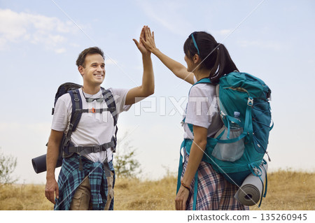 Hikers couple high-fiving on forest trail, smiling with backpacks and gear Hikers couple high-fiving on forest trail, smiling with backpacks and gear 135260945