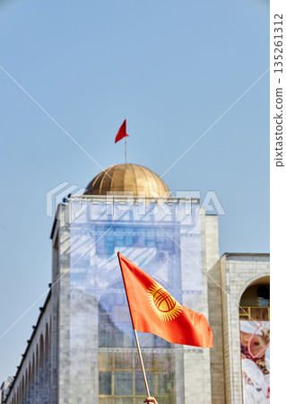 Arm holding Kyrgyz flag, with a building dome and red flag. National patriotism Arm holding Kyrgyz flag, with a building dome and red flag. National patriotism 135261312