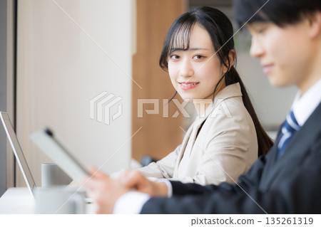 A young woman using a laptop computer in a calm and stylish cafe or office space, looking at the camera and smiling 135261319