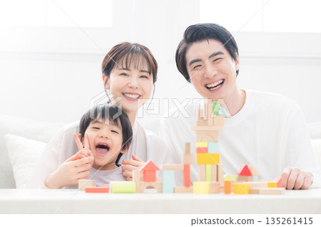 A smiling family looking at the camera in front of building blocks, conveying happiness. Family image of child-rearing, including education and childcare. A smiling family looking at the camera in front of building blocks, conveying happiness. Family image of child-rearing, including education and childcare. 135261415