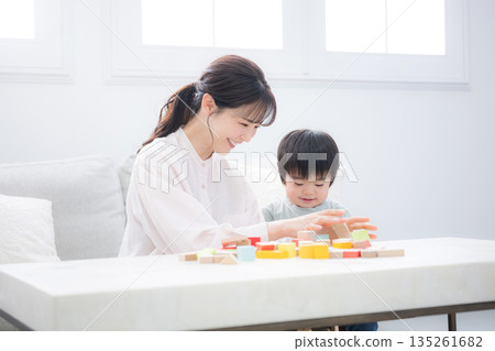 Smiling 2-year-old and mother playing with building blocks. Image of education, such as intellectual development. Kindergarten entrance exams, etc. Smiling 2-year-old and mother playing with building blocks. Image of education, such as intellectual development. Kindergarten entrance exams, etc. 135261682