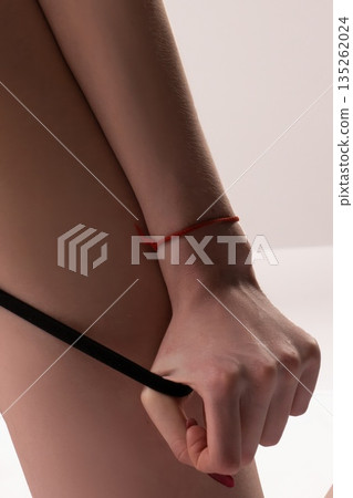 Woman's arm and hand gripping a black strap, wearing a red string bracelet Woman's arm and hand gripping a black strap, wearing a red string bracelet 135262024