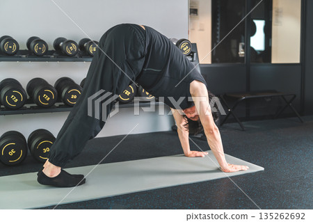 Young Asian man doing yoga and stretching exercises in training gym 135262692