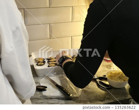 Woman preparing mussels in a white dish. Culinary activity for home cooking and gourmet food preparation. Seafood cooking concept. Woman preparing mussels in a white dish. Culinary activity for home cooking and gourmet food preparation. Seafood cooking concept. 135263622