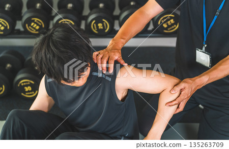 一名肩部疼痛的男子正在訓練,以及一名男性運動物理治療師 一名肩部疼痛的男子正在訓練,以及一名男性運動物理治療師 135263709