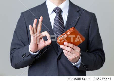 A middle-aged male businessman in a suit holding a wallet and making a circle sign A middle-aged male businessman in a suit holding a wallet and making a circle sign 135265361