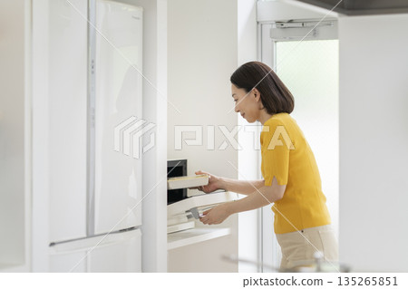 A woman in her 50s warming up her lunch in the microwave A woman in her 50s warming up her lunch in the microwave 135265851