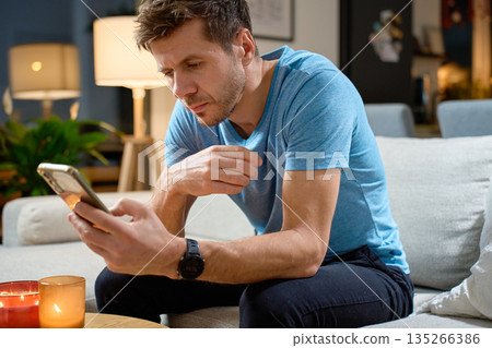 Man sitting on sofa and using smartphone at home 135266386