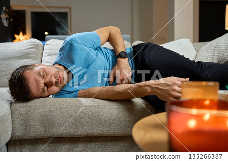 Man lying on sofa with stomach pain at home 135266387