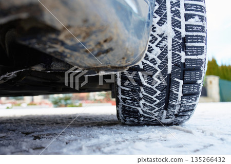 Winter car tire with snow on tread on icy road 135266432